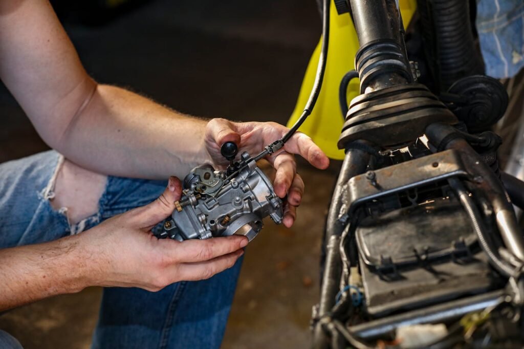 Close-up shot of a mechanic's hands repairing a motorcycle carburetor indoors.